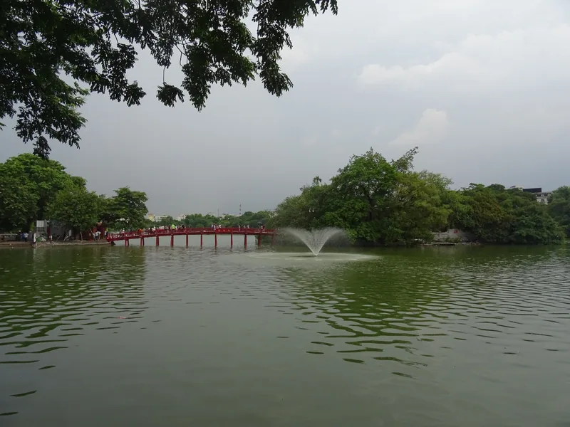 Cầu Thê Húc màu đỏ bắc qua Hồ Hoàn Kiếm ở Hà Nội, với đài phun nước giữa mặt hồ xanh.