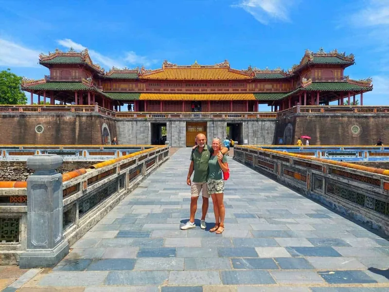 Hai du khách chụp ảnh trên cầu dẫn vào cổng Ngọ Môn của Đại Nội Huế dưới bầu trời xanh.