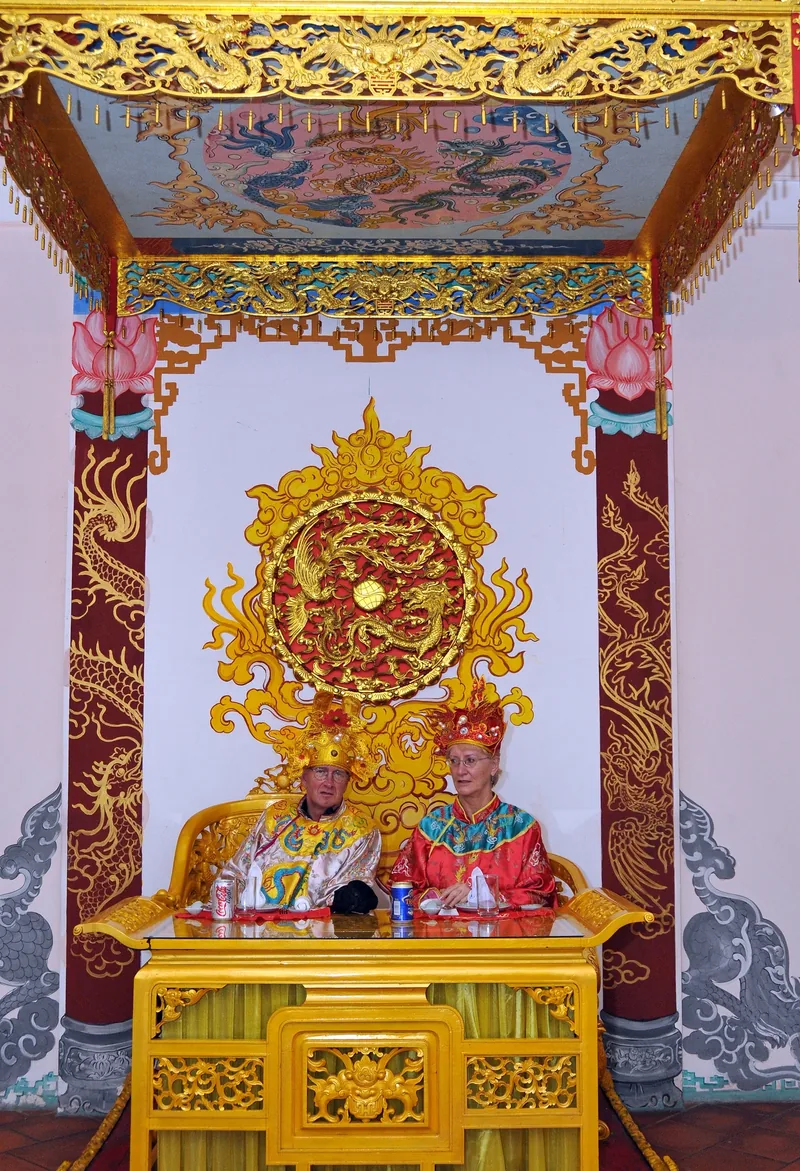 Du khách mặc trang phục vua và hoàng hậu triều Nguyễn ngồi trên ngai vàng dưới các họa tiết rồng ở Huế.