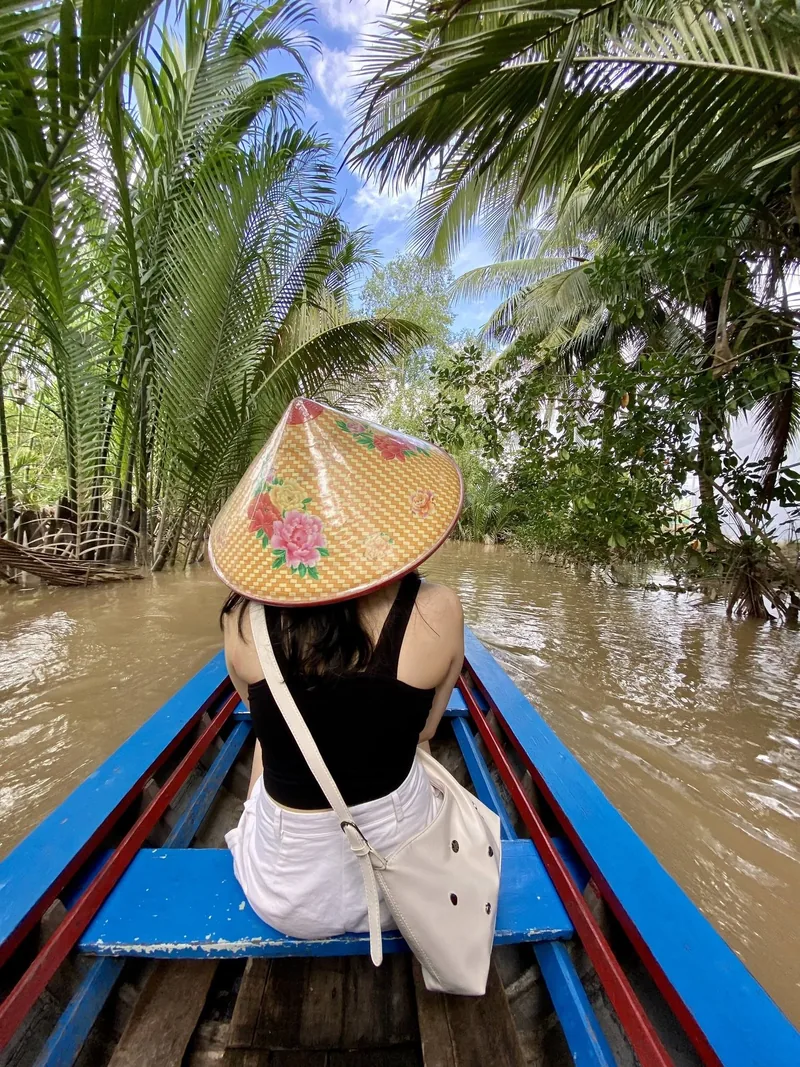 Một phụ nữ đội nón lá ngồi trên xuồng nhỏ len lỏi qua kênh rạch rợp bóng dừa ở đồng bằng sông Mekong.