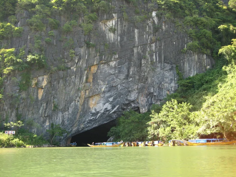 Những chiếc thuyền gỗ chở khách tập trung tại cửa động Phong Nha dưới vách núi đá vôi cao lớn.