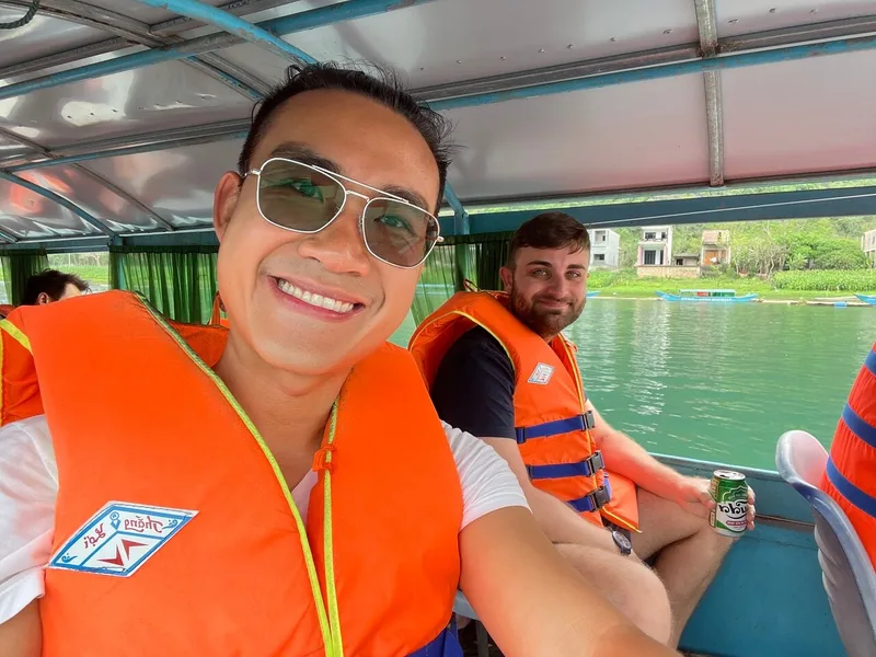 Du khách mặc áo phao cam cười tươi chụp ảnh selfie trên thuyền đi vào Động Phong Nha.