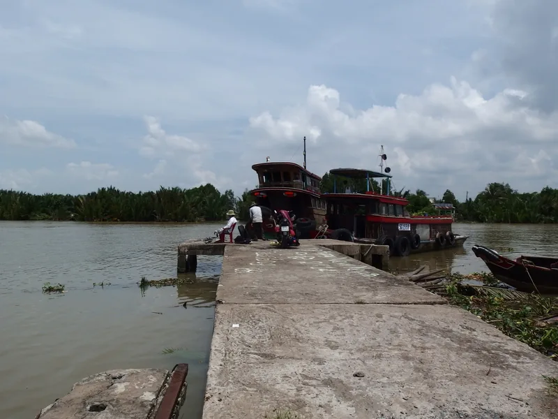 Những chiếc thuyền gỗ chở hàng neo đậu bên bến bê tông trên dòng sông nước đục vùng đồng bằng sông Cửu Long.